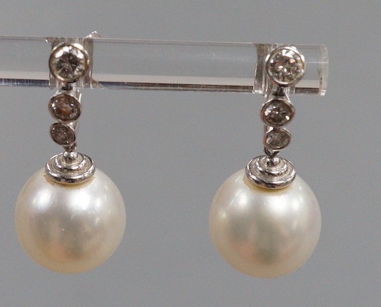 A modern pair of 750 white metal, singe stone South Sea pearl and graduated three stone diamond set drop earrings, overall 22mm, gross weight 6.8 grams